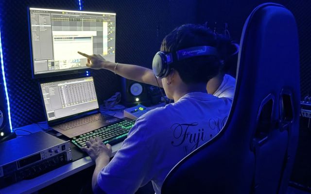 Un ingeniero de audio imparte una formación a un alumno utilizando auriculares Sennheiser, monitores duales, Ableton Live, un teclado mecánico RGB y tratamiento acústico.